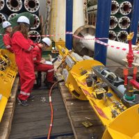 Scientists with hardhats work on a heavy instrument before deployment at sea