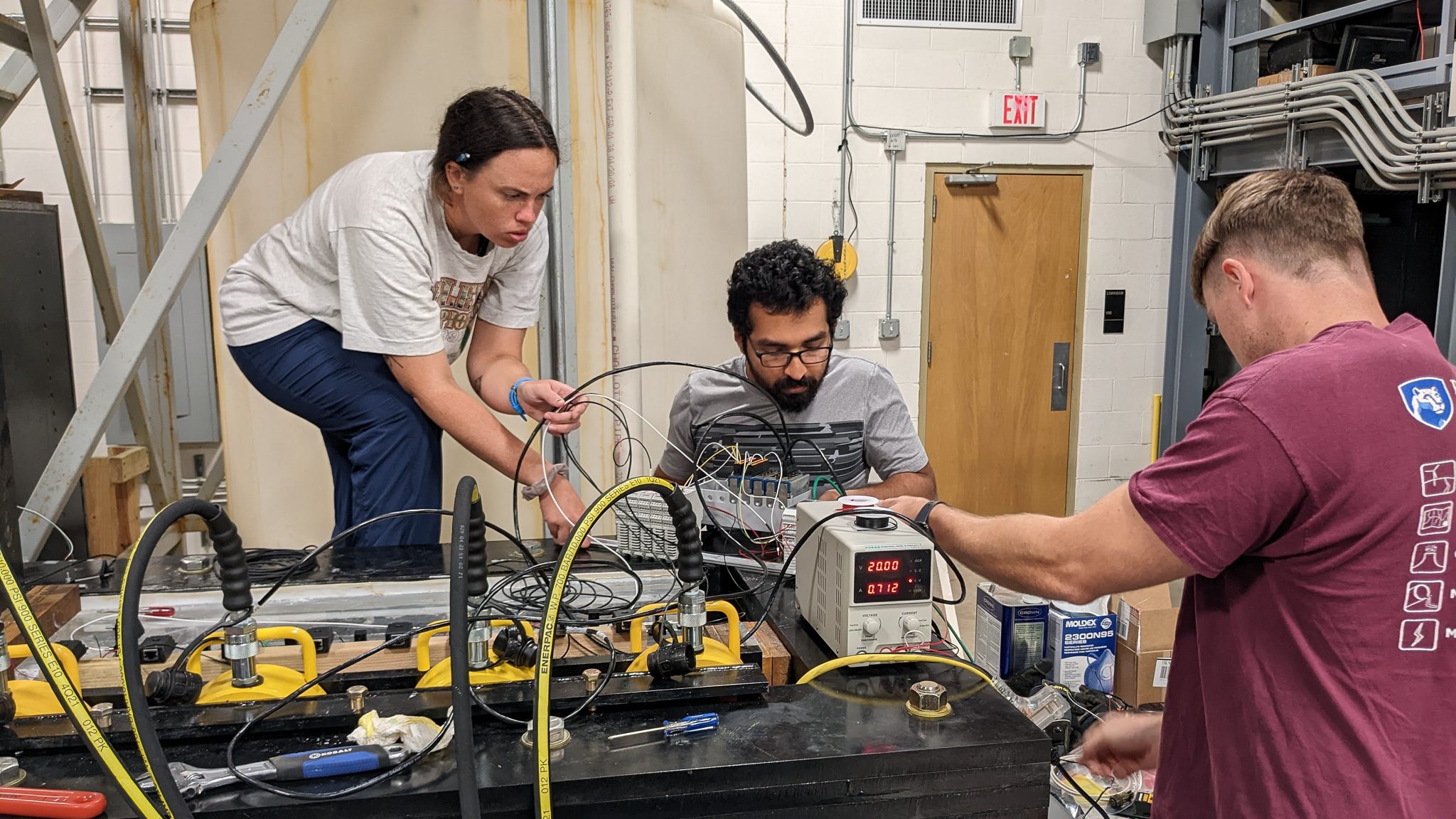 The researchers are crowded around the apparatus each busy with a different part.