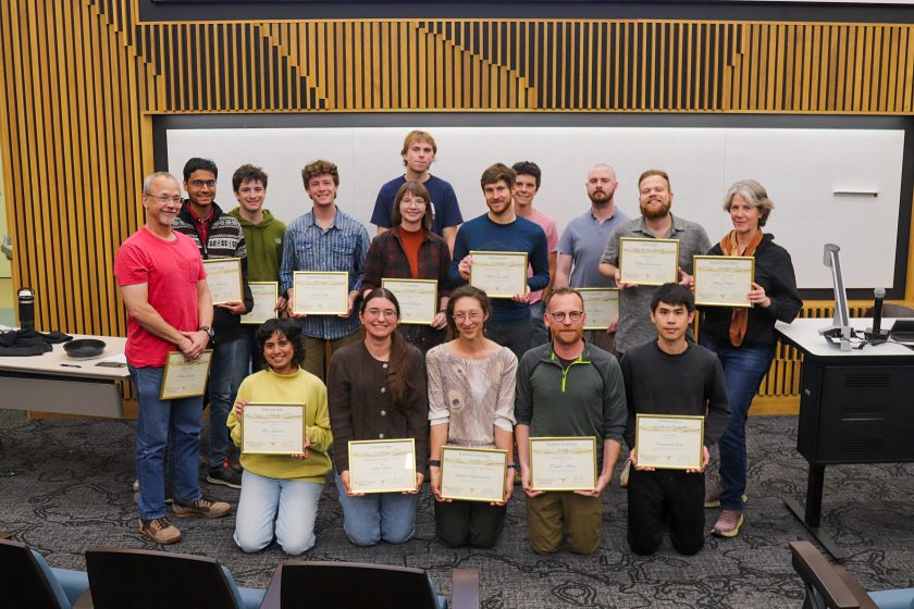 A group of people stand and kneel in two rows holding certificates.