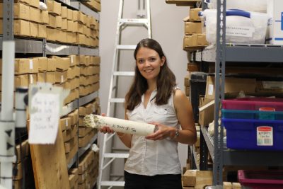 Picture of Allison holding a bone-like coral with stacked cardboard containers either side indicating she is in a warehouse 