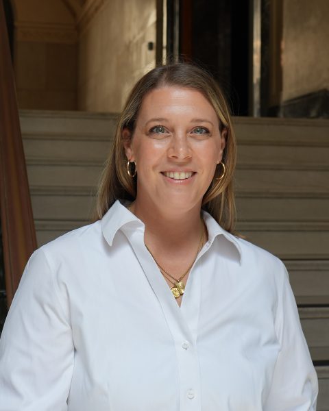 A woman in a white shirt smiles in near a set of stairs in the UT tower building