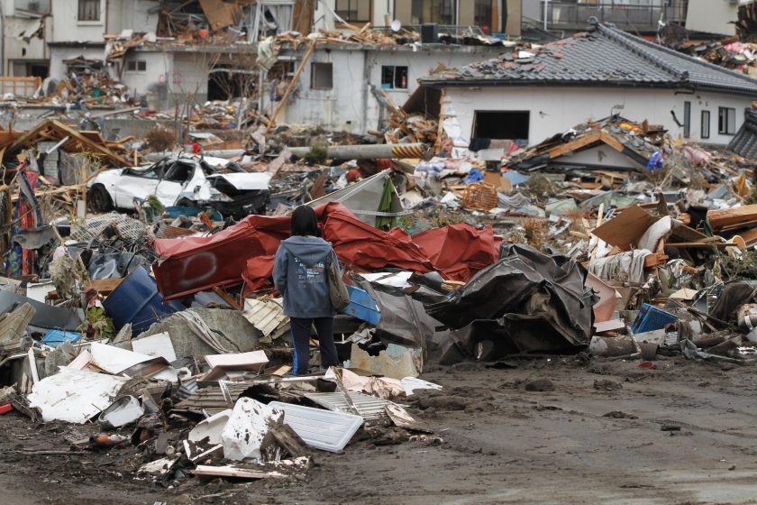 A child stands among ruined buildings with her back to the camera.