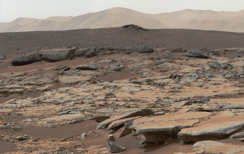 A photo of Mars' surface, with pieces of flat rock in the foreground and mountains in the background.