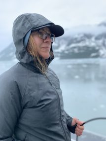 A profile portrait of Ginny Catania at sea with a glacier and ice floes in the background