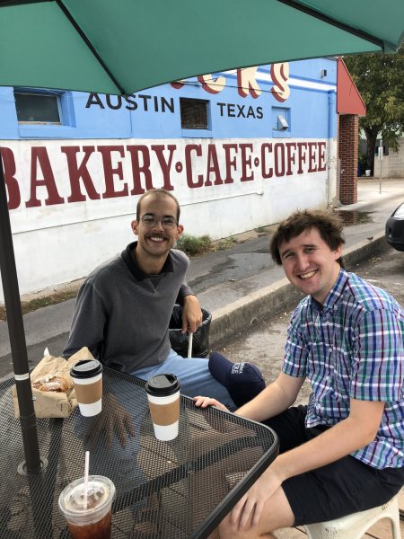 Ethan and Edward sitting at a table outside the cafe smiling at the camera.