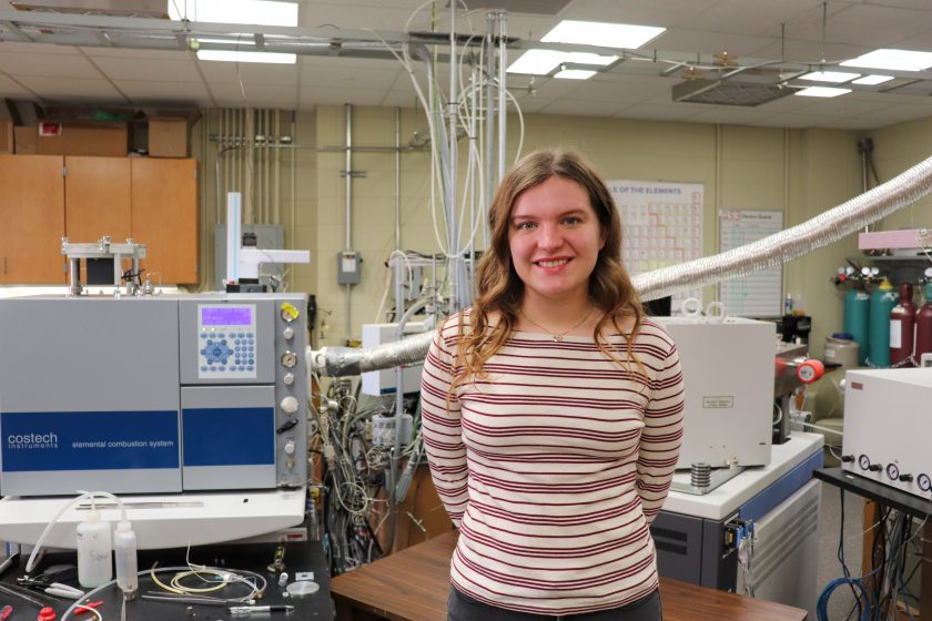 A woman wearing a striped shirt stands in front of lab equipment.
