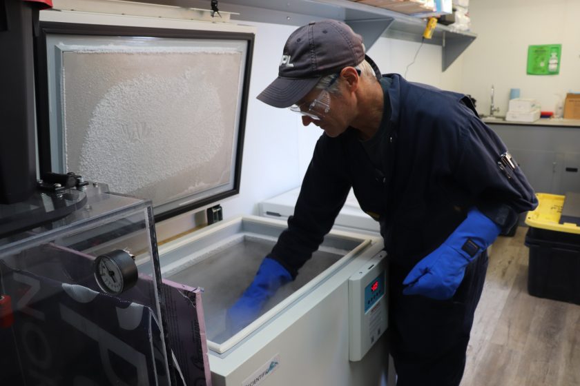 Photo of Rick wearing protective gear and reaching into a chest freezer.