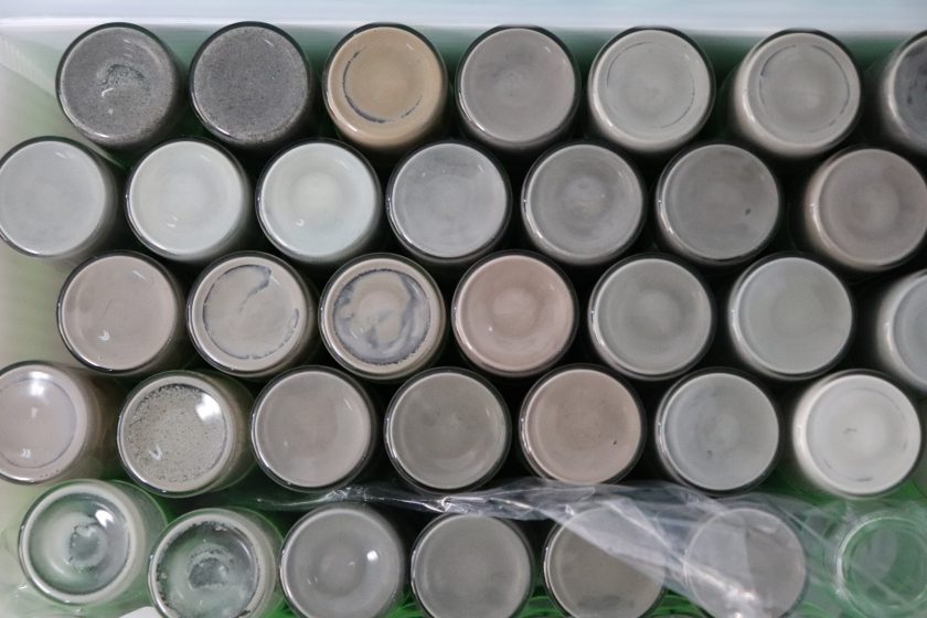 Top-down view on glass containers holding greyish sediments. There are around 30 containers in neat rows.