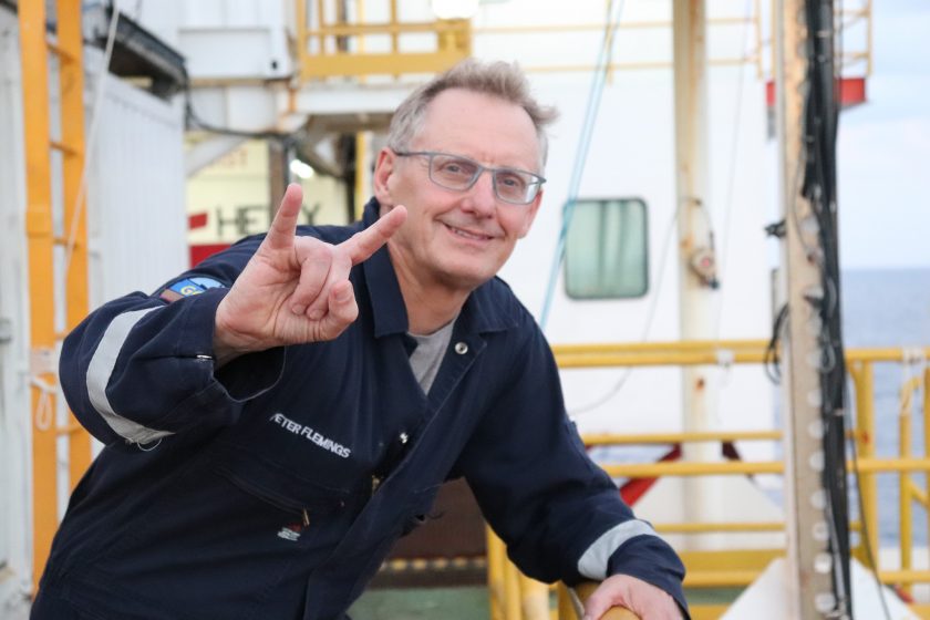 Photo of Peter leaning on the side of the deck with one hand raised flashing a hook 'em at the camera.