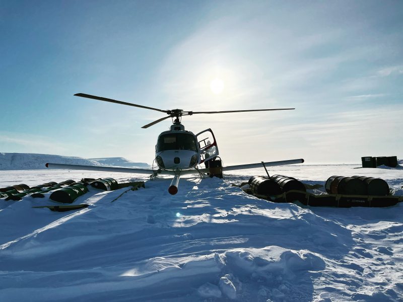 Photo of a helicopter on an icy landscape with the sun behind it. 