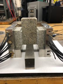 Photo of three granite-like blocks in an instrument that looks like a metal vice, connected to thick heavy cables.