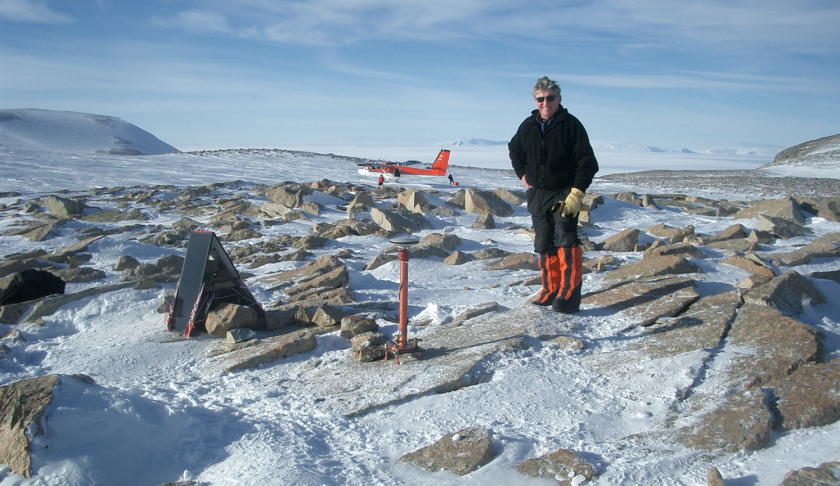 A picture showing Ian Dalziel standing among snow and rocks with a deployed sensor ahead of him. In the background is a landed Twin Otter aircraft.