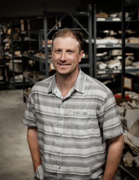 Ben Kligman in the foreground with rows of shelves packed with fossils in the background.