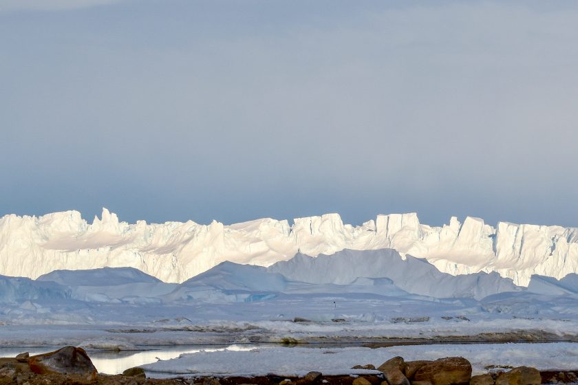 A wall of ice one the horizon with some coastal water in the foreground