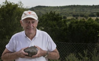 Leon Long, professor emeritus of geology at the University of Texas, holds a volcanic rock sample from the ancient volcano known as Pilot Knob seen in the background in Southeast Austin