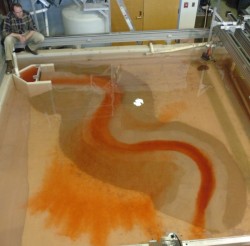 Mohrig discovered that underwater currents follow sea floor channels, even when the current is much larger than the channel. The water current in this sand table experiment is dyed red. Larger image.