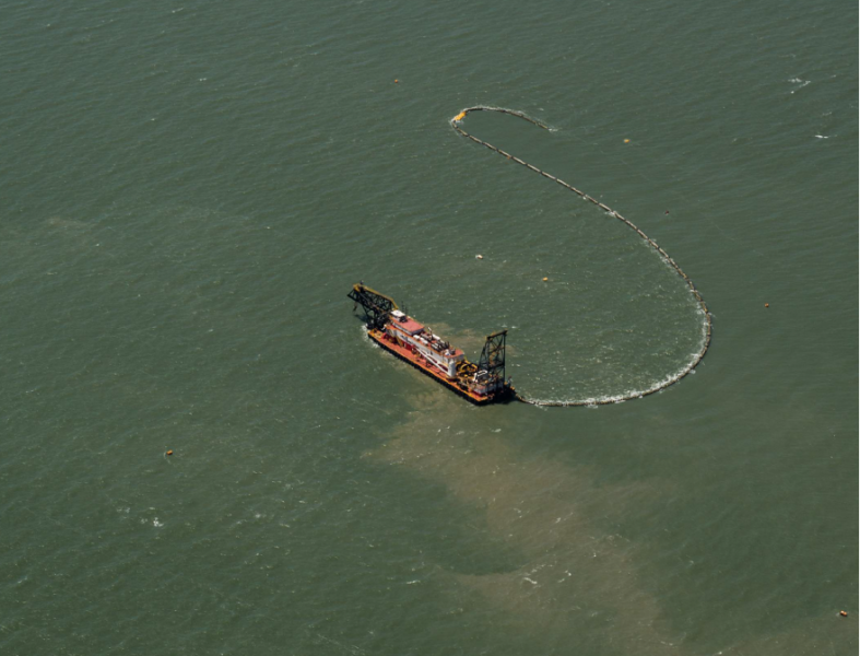 An aerial view of a dredging vessel at sea. Trails of sand are visible in vessel's wake.