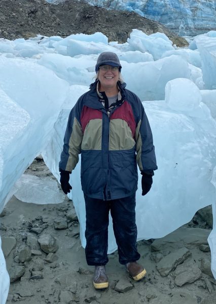 Gail Christeson at the foot of a glacier surrounded by blue ice and mountains.